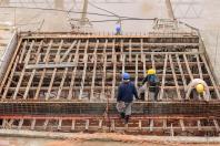 Quatro trabalhadores usando capacetes, na construção, mexendo com madeiras.