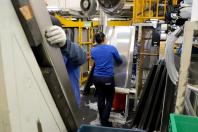 Mulher vestida de azul e preto, cabelos presos, trabalhando em fábrica, em meio a maquinários e ferramentas.