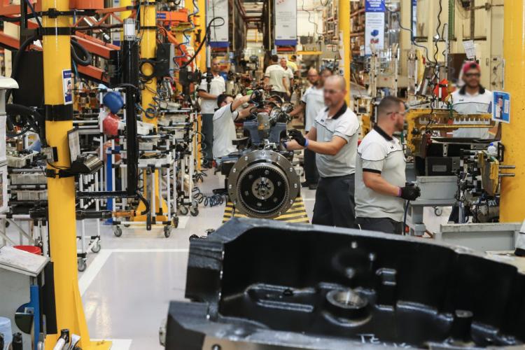 Imagem interna de uma fábrica, com trabalhadores na linha de montagem