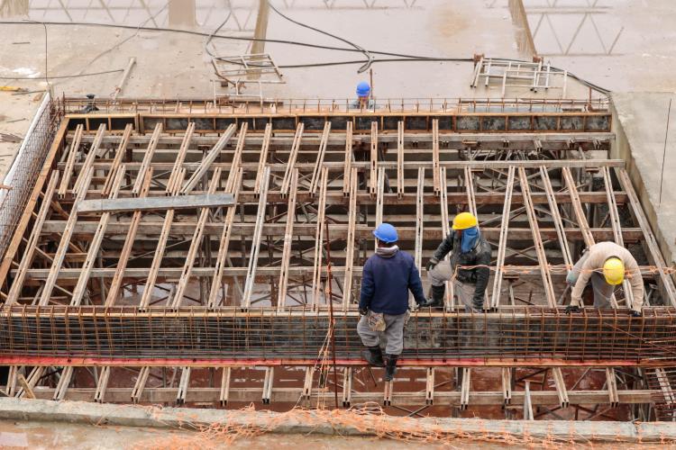 Quatro trabalhadores usando capacetes, na construção, mexendo com madeiras.